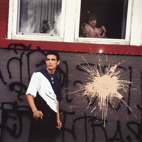 man standing next to wall with splattered paint; girl looking out from window above