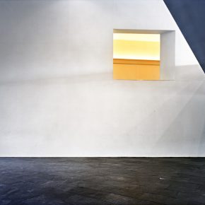 white wall; large, empty window; yellow light coming through
