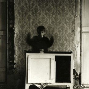 child in motion with hands raised, standing behind cabinet in decaying house