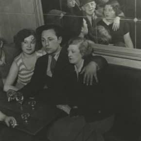man with two women on either side of him at a bar; people sitting across from them are reflected in mirror