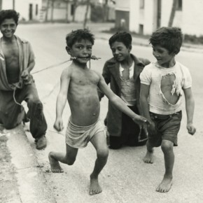 four boys playing outside; shirtless boy is pretending he is a horse